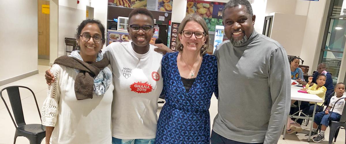 Shalini Kulasingam, Waruiru Mburu, Beth Virnig, and John Amuasi smile at the camera, standing in a restaurant in Ghana