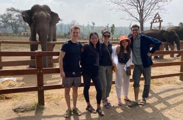 Five students stand in front of an elephant, facing the camera and smiling
