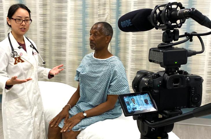 While filming for the IOM online training materials, a doctor stands next to a patient, who is sitting on an exam table. The doctor is facing a camera and mid-sentence while the patient looks straight ahead.