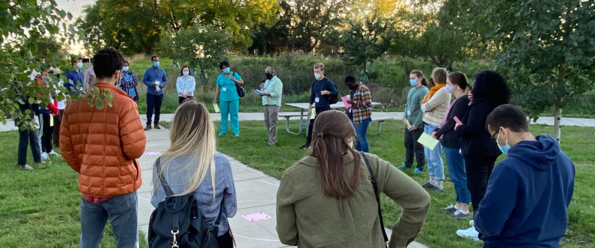Students in the Global Local course stand in a circle outside while listening to a professor. 