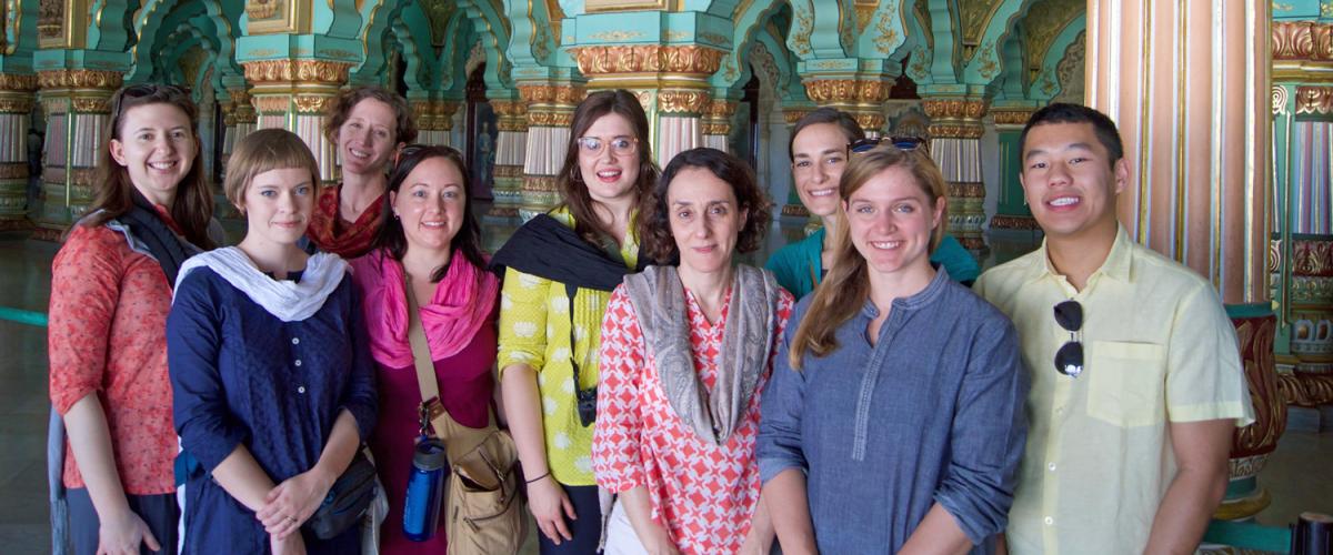 Inside Mysore Palace, students in the 2018 India course stand looking at the camera with intricate detailing behind them.
