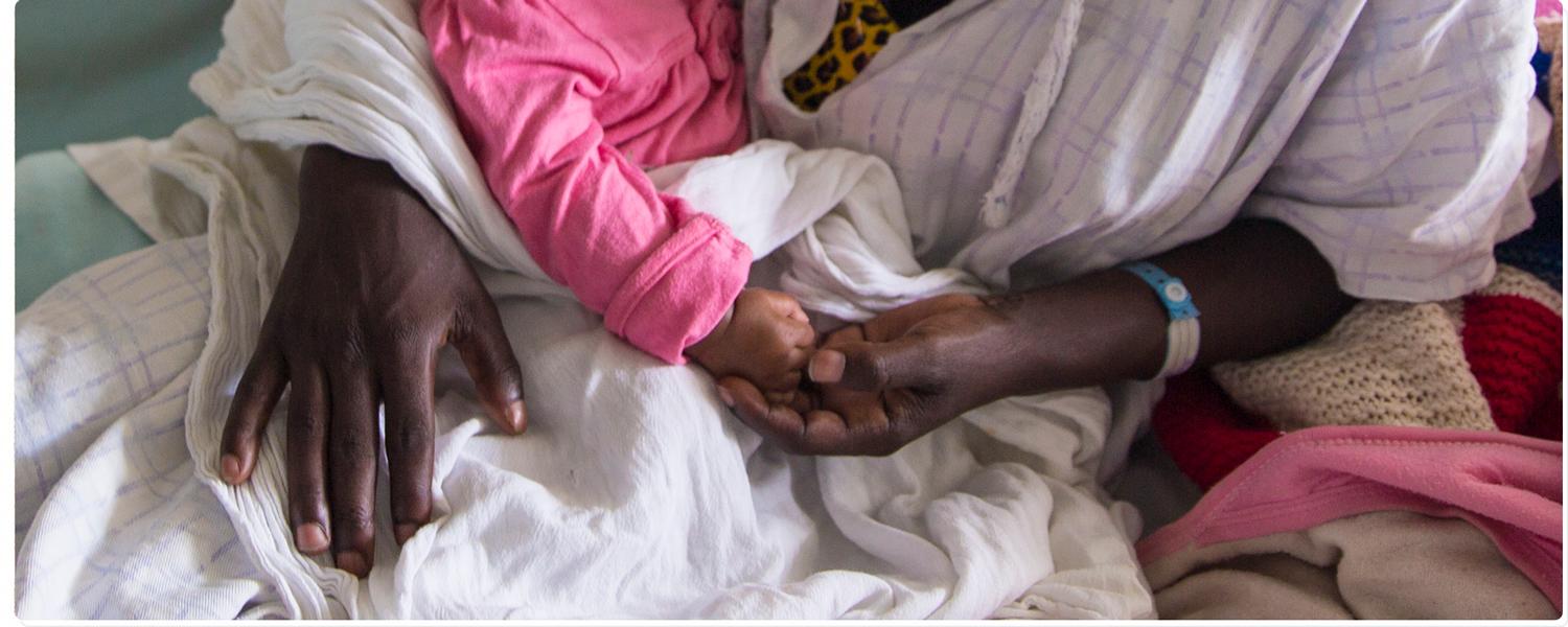 A mother holds her baby in a hospital in Ethiopia, photo is cropped to show only their hands
