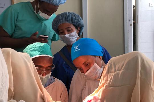 Four physicians look over a woman while performing surgery