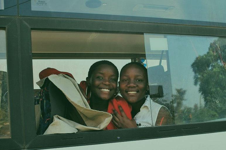 Two IOM nurses on a bus look out the bus window, smiling toward the camera